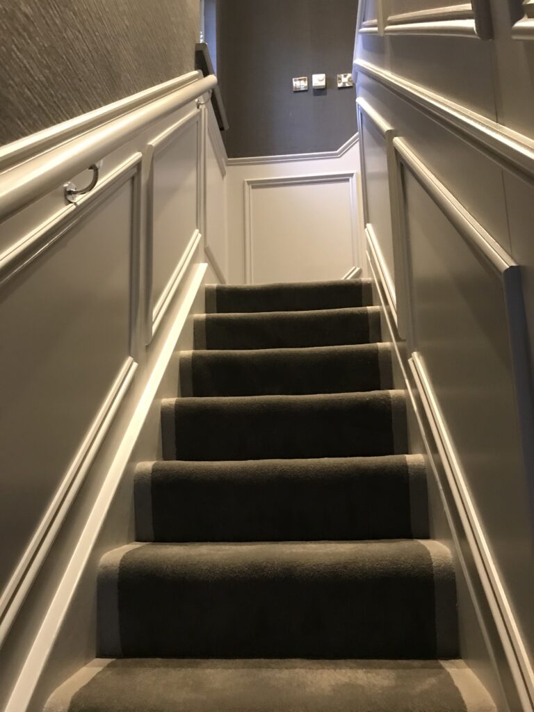 White staircase with a gray carpet in a modern home , leading towards a landing area where multiple wall switches are present.