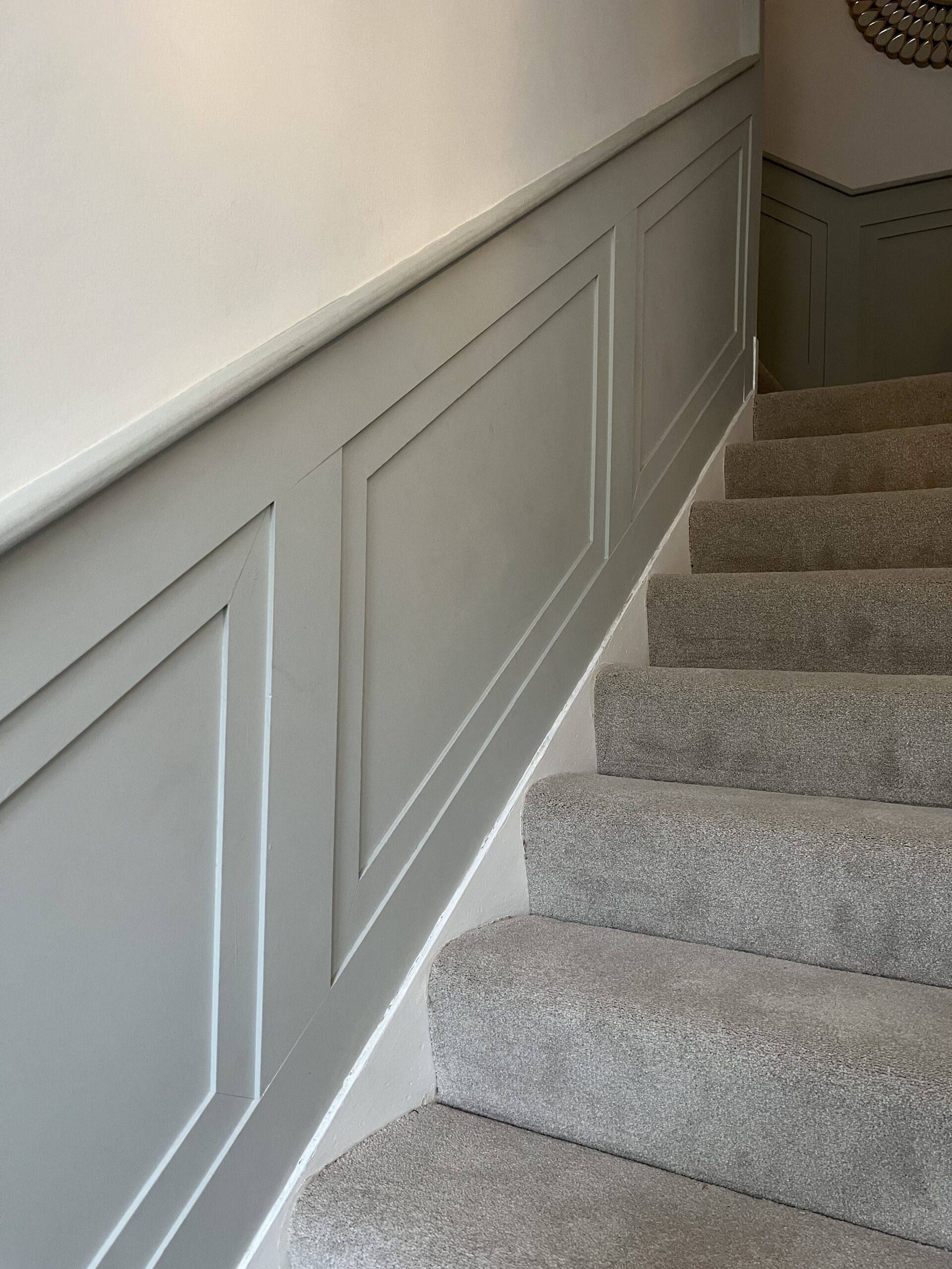 Painted wall panelling alongside a carpeted staircase